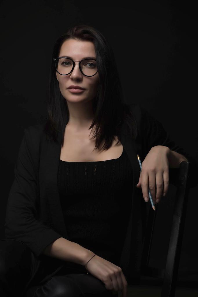 Ирина Панчурина, архитектор-дизайнер, сидит с карандашом в руке на тёмном фоне